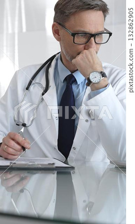 Male doctor in lab coat and stethoscope working on laptop, providing medical consultation in a modern clinic office. Medicine and health care Male doctor in lab coat and stethoscope working on laptop, providing medical consultation in a modern clinic office. Medicine and health care 132862905