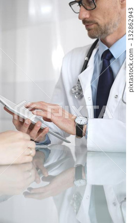 Male doctor consulting female patient, discussing diagnosis and medical history with digital tablet in clinic. Medicine and health care 132862943