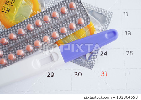 Pregnancy test with birth control pills and condom for female on calendar, ovulation day. Pregnancy test with birth control pills and condom for female on calendar, ovulation day. 132864558