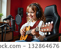 A girl with headphones and a guitar sits at the microphone in a recording studio 132864676