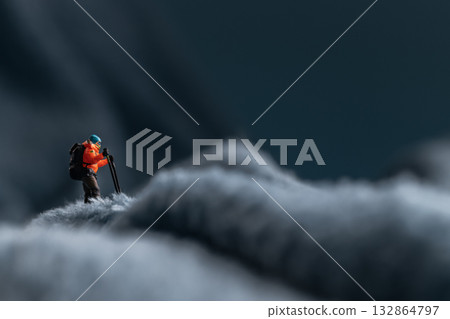 A miniature mountain climber figurine on a fuzzy fleece lining resembling a snow-covered surface, with a blurred background of a mountain or ice wall 132864797