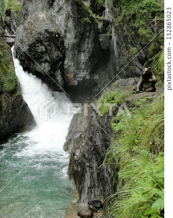 A  stream of clear water, a waterfall flows down from high mountains down over rocks between high mountains 132865023