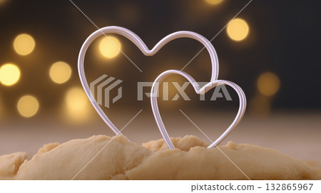 Two heart-shaped metal cookie cutters placed on raw dough, with warm bokeh lights in the background suggesting romance or holidays. Two heart-shaped metal cookie cutters placed on raw dough, with warm bokeh lights in the background suggesting romance or holidays. 132865967