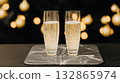 Two glasses of sparkling champagne stand on a marble tray with warm glowing lights in the background, evoking holiday celebration.  132865974