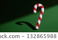 Classic red and white candy cane casting a bold shadow on a green background, minimal Christmas concept with dramatic light.  132865988