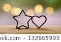 A black star and heart cookie cutter pair stands upright on a wooden surface with warm, glowing bokeh in the background.  132865993