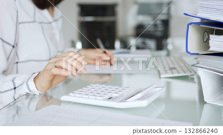 Woman working in office, calculating finances with white calculator, managing accounting paperwork and business expenses. Audit and taxes in business 132866240