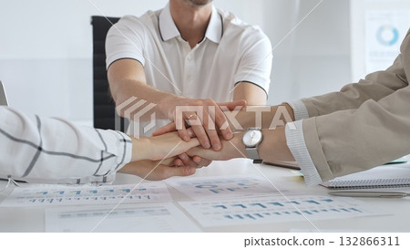 Business people joining hands over workplace documents, symbolizing collaborative spirit and shared workplace success 132866311