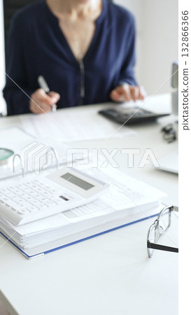 Professional analyzing financial data, writing notes near laptop, magnifying glass, documents, binders on workplace desk. Audit and taxes concept Professional analyzing financial data, writing notes near laptop, magnifying glass, documents, binders on workplace desk. Audit and taxes concept 132866366