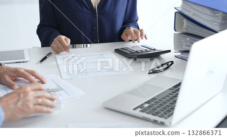 Business team of business man and female entrepreneur analyzing financial documents, using calculators and laptop, working together on project in modern office. Audit and taxes concept 132866371