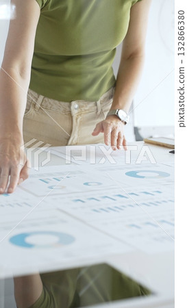 Businesswoman pointing at financial charts and graphs on a table, with a pie chart on a flip chart in the background. Business people concept Businesswoman pointing at financial charts and graphs on a table, with a pie chart on a flip chart in the background. Business people concept 132866380