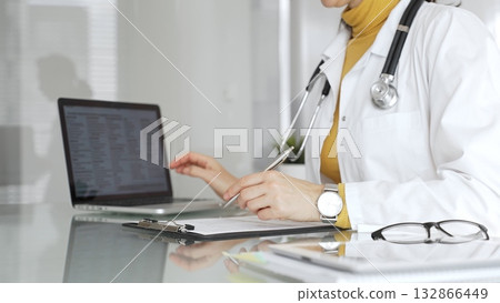 Doctor working on medical records, writing prescription in clinic office, using laptop for patient data management. Medicine, healthcare and science concept 132866449
