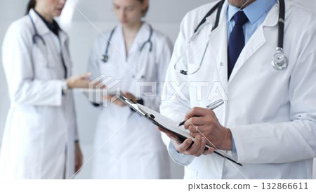 During a discussion with the medical team, a physician takes notes on a clipboard, capturing aspects of collaborative patient care, documentation, and clinical healthcare strategies 132866611