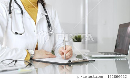 Female physician or medic completing paperwork, preparing a diagnosis, or providing healthcare service in a clean modern office. Medicine, healthcare and science concept Female physician or medic completing paperwork, preparing a diagnosis, or providing healthcare service in a clean modern office. Medicine, healthcare and science concept 132866612