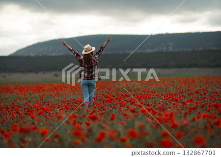 Woman poppy field arms raised standing in vast red flowers under a cloudy sky expressing freedom 132867701