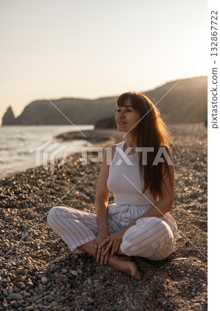 Woman, beach, sunset. Young woman relaxing peacefully on a pebble beach, enjoying the beautiful golden hour light by the sea Woman, beach, sunset. Young woman relaxing peacefully on a pebble beach, enjoying the beautiful golden hour light by the sea 132867722