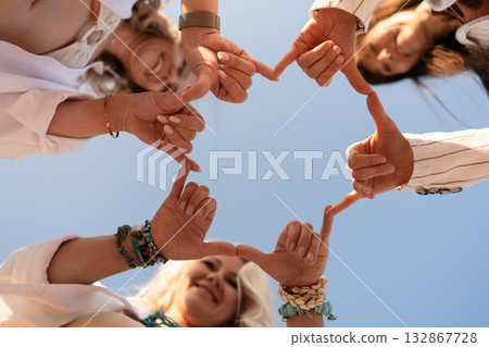 Hands, friendship, teamwork. Four women form a square shape with fingers against clear blue sky, symbolizing unity and connection. Hands, friendship, teamwork. Four women form a square shape with fingers against clear blue sky, symbolizing unity and connection. 132867728