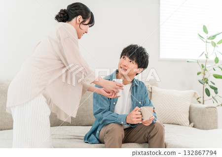 一對年輕的亞洲夫婦坐在家裡的客廳沙發上，一邊看著智慧型手機一邊聊天。 132867794