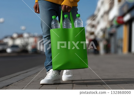 Person carrying a green bag filled with empty plastic bottles while walking on the street Person carrying a green bag filled with empty plastic bottles while walking on the street 132868000