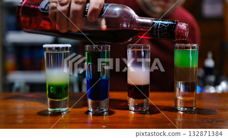 Professional male bartender pouring mixed blue liquor cocktail drink from cocktail shaker into shot glass on bar counter at nightclub. Mixologist barman making alcoholic drink serving to customer Professional male bartender pouring mixed blue liquor cocktail drink from cocktail shaker into shot glass on bar counter at nightclub. Mixologist barman making alcoholic drink serving to customer 132871384
