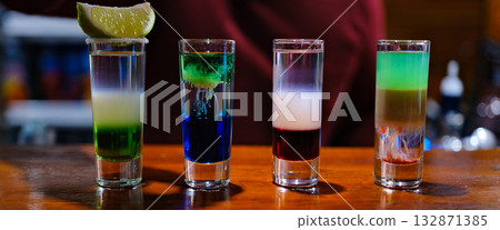 Vibrant layers of colorful shots display a creative mixology masterpiece. Each glass captures light beautifully while showcasing a spectrum of colors, igniting excitement in a lively bar atmosphere. Vibrant layers of colorful shots display a creative mixology masterpiece. Each glass captures light beautifully while showcasing a spectrum of colors, igniting excitement in a lively bar atmosphere. 132871385