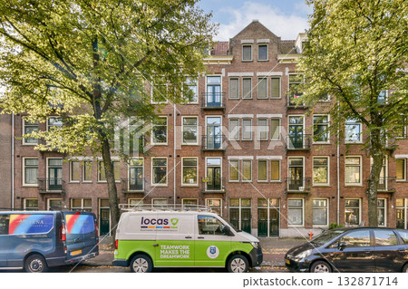 A picturesque urban landscape showcasing a charming building adorned with large windows, framed by vibrant trees and parked vehicles, capturing suburban tranquility. A picturesque urban landscape showcasing a charming building adorned with large windows, framed by vibrant trees and parked vehicles, capturing suburban tranquility. 132871714