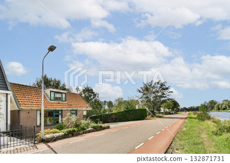 A picturesque road lined with vibrant greenery and a charming house, perfect for a peaceful countryside stroll or bike ride. The clear blue sky adds to the tranquility. A picturesque road lined with vibrant greenery and a charming house, perfect for a peaceful countryside stroll or bike ride. The clear blue sky adds to the tranquility. 132871731