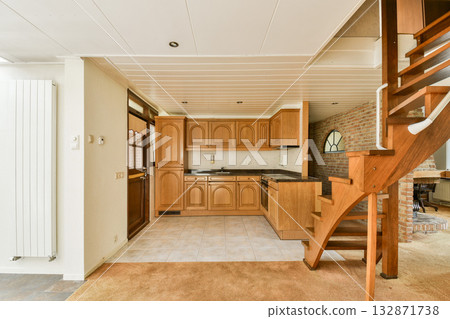 A bright, modern kitchen showcasing wooden cabinetry and a stylish staircase. The design combines functionality with elegant aesthetics in a welcoming space. A bright, modern kitchen showcasing wooden cabinetry and a stylish staircase. The design combines functionality with elegant aesthetics in a welcoming space. 132871738