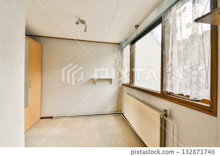 A bright and minimalist room featuring large windows allowing natural light, a simple closet, and neutral-colored walls, offering a clean aesthetic. 132871740