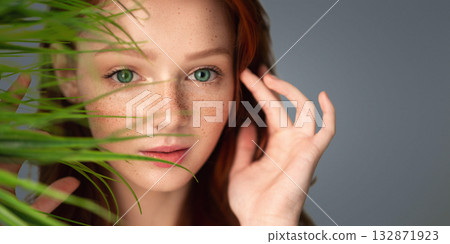 Natural Haircare. Ginger-Haired Young Woman Touching Red Hair Posing With Green Plant Leaves Near Face On Gray Background In Studio. Beauty And Facial Skin Care Cosmetics. Selective Focus Natural Haircare. Ginger-Haired Young Woman Touching Red Hair Posing With Green Plant Leaves Near Face On Gray Background In Studio. Beauty And Facial Skin Care Cosmetics. Selective Focus 132871923