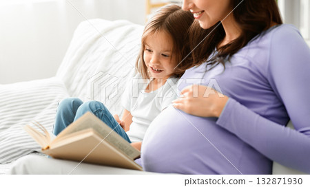 Close up of excited little girl reading book with expecting mom, home interior, copy space 132871930