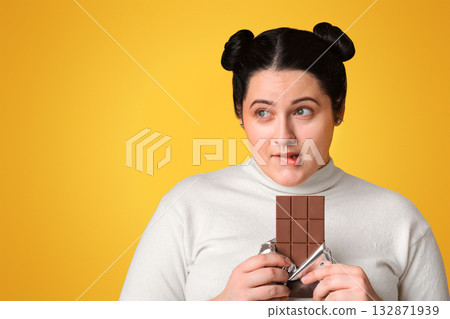 Sugar Addiction Concept. Young Obese Girl Cannot Resist Temptation To Eat Chocolate, Standing Over Yellow Background With Pensive Face Expression 132871939