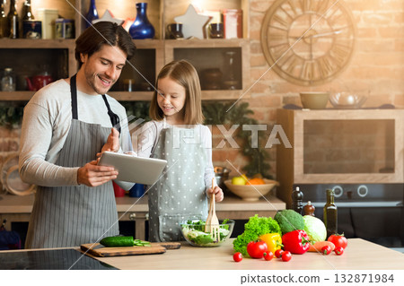 Best Recipe Apps. Cheerful young father and his little daughter using digital tablet in kitchen, choosing what to cook 132871984