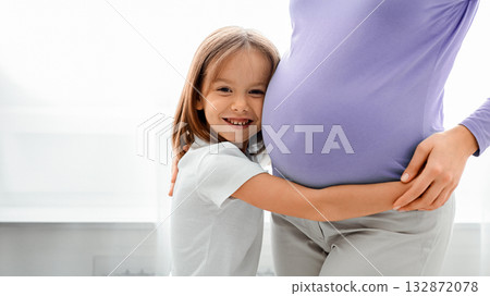 Close up of excited little daughter embracing her pregnant mom, white background 132872078