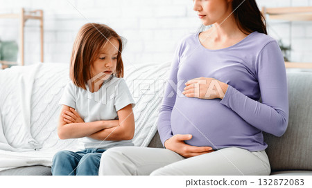 Close up of upset little daughter looking at her pregnant mom belly, family issue Close up of upset little daughter looking at her pregnant mom belly, family issue 132872083