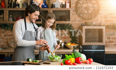 Young father and daughter cooking meal together, adding seasoning to salad, enjoying spending time in kitchen 132872203