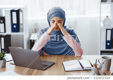 Exhausted arabic businesswoman having migraine after long time work in office, sitting at desk and touching her nose bridge, having bad day Exhausted arabic businesswoman having migraine after long time work in office, sitting at desk and touching her nose bridge, having bad day 132872324