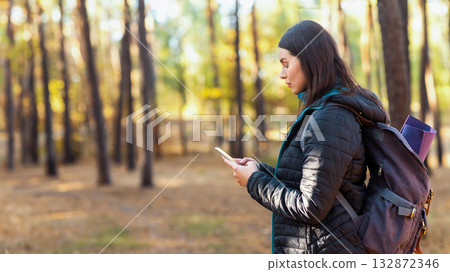 Side view of serious girl with backpack using mobile phone in forest, checking location, copy space Side view of serious girl with backpack using mobile phone in forest, checking location, copy space 132872346