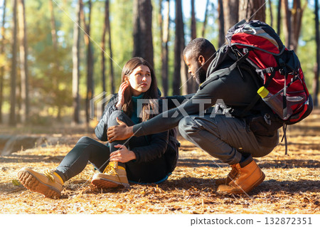 African guy comforting his caucasian pretty girlfriend hurt her ancle while camping in forest, free space 132872351