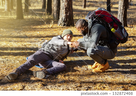 Black guy helping his injured friend while camping by pine forest, copy space Black guy helping his injured friend while camping by pine forest, copy space 132872408