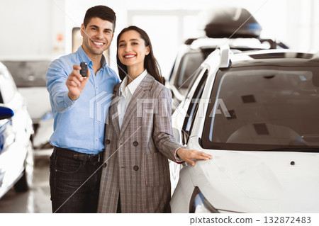 New Car Owners. Young Famile Standing In Dealership Store, Man Showing New Car Key, Free Space New Car Owners. Young Famile Standing In Dealership Store, Man Showing New Car Key, Free Space 132872483