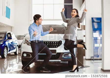 Happy Car Owners. Joyful Couple Celebrating Buying Auto Shaking Fists Jumping Standing In Automobile Dealership Showroom Happy Car Owners. Joyful Couple Celebrating Buying Auto Shaking Fists Jumping Standing In Automobile Dealership Showroom 132872508
