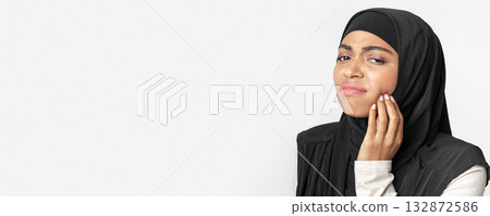 Toothache concept. Black muslim woman in headscarf suffering from teeth pain, touching her inflamed cheek, gray background with free space, panorama 132872586