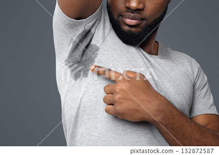 Cropped of young afro man looking at the sweaty shirt, white background, copy space, wet armpit problem 132872587