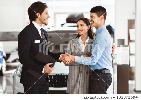 Fair Deal. Happy Man Shaking Hands With Car Sales Manager Buying Auto With Wife In Automobile Dealership Store Fair Deal. Happy Man Shaking Hands With Car Sales Manager Buying Auto With Wife In Automobile Dealership Store 132872594