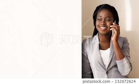 African American Businesswoman Talking On Smartphone Near Window In Office, Leaning On Wall, Having Break. Panorama With Copy Space African American Businesswoman Talking On Smartphone Near Window In Office, Leaning On Wall, Having Break. Panorama With Copy Space 132872624