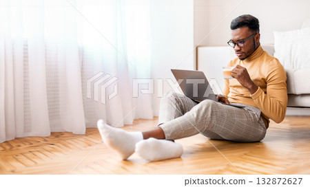 Freelance Career. Serious Black Freelancer Guy Working On Laptop Computer And Having Coffee Sitting On Floor At Home. Selective Focus Freelance Career. Serious Black Freelancer Guy Working On Laptop Computer And Having Coffee Sitting On Floor At Home. Selective Focus 132872627
