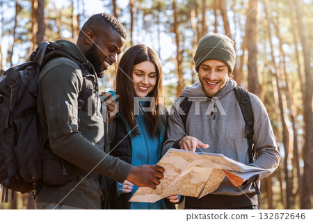 Multiracial friends with backpacks looking at map, hiking in autumn forest 132872646