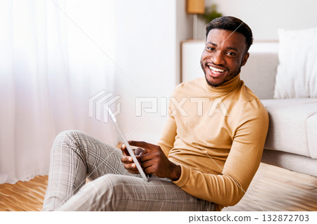 Black Guy Using Tablet Computer Smiling At Camera Sitting On Floor At Home. Selective Focus 132872703