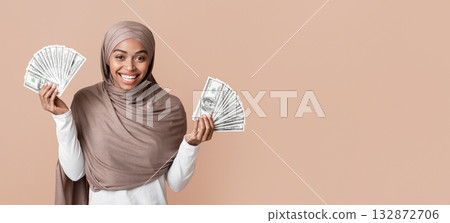 Lucky Winner. Overjoyed Black Muslim Girl in Hijab Holding Lots Of Dollar Cash In Both Hands, Standing Over Yellow Background With Free Space Lucky Winner. Overjoyed Black Muslim Girl in Hijab Holding Lots Of Dollar Cash In Both Hands, Standing Over Yellow Background With Free Space 132872706